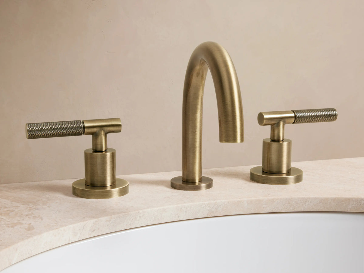 Crewe Knurled Faucet in antique brass finish, featuring an arched spout and two knurled handles, mounted on a dark countertop.