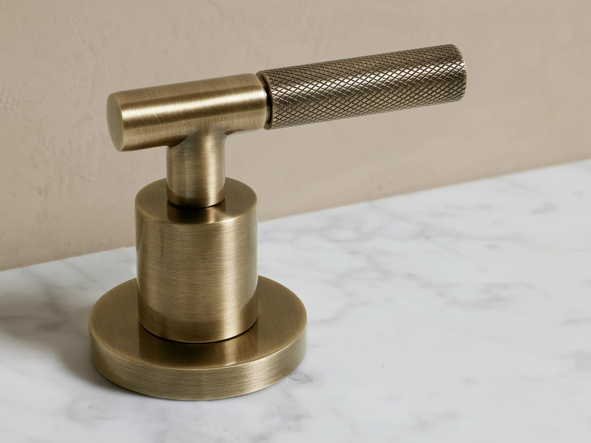 Crewe Knurled Faucet in antique brass with arched spout and two textured handles, mounted on a white countertop.