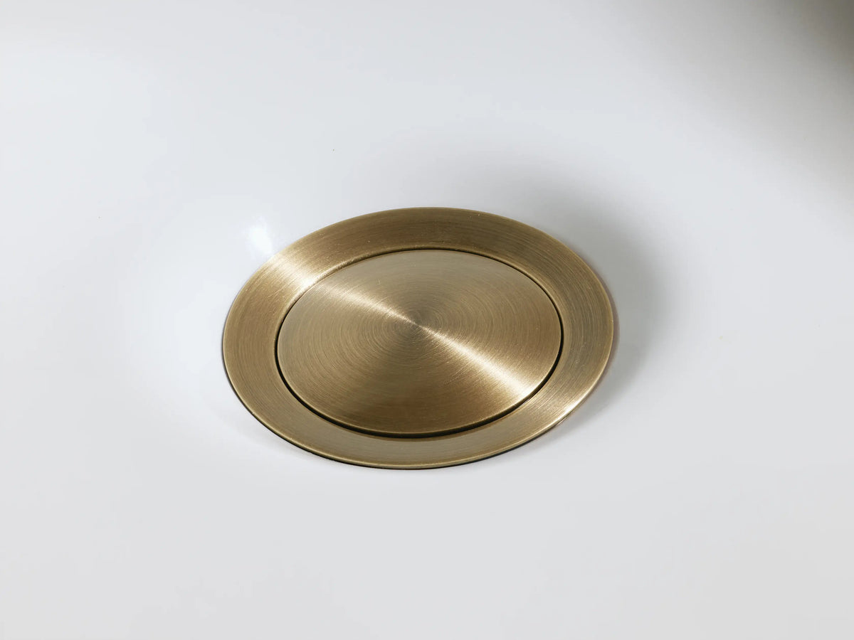 Knurled antique brass handle of the Crewe Knurled Faucet resting on a marble countertop with a textured finish against a beige background.