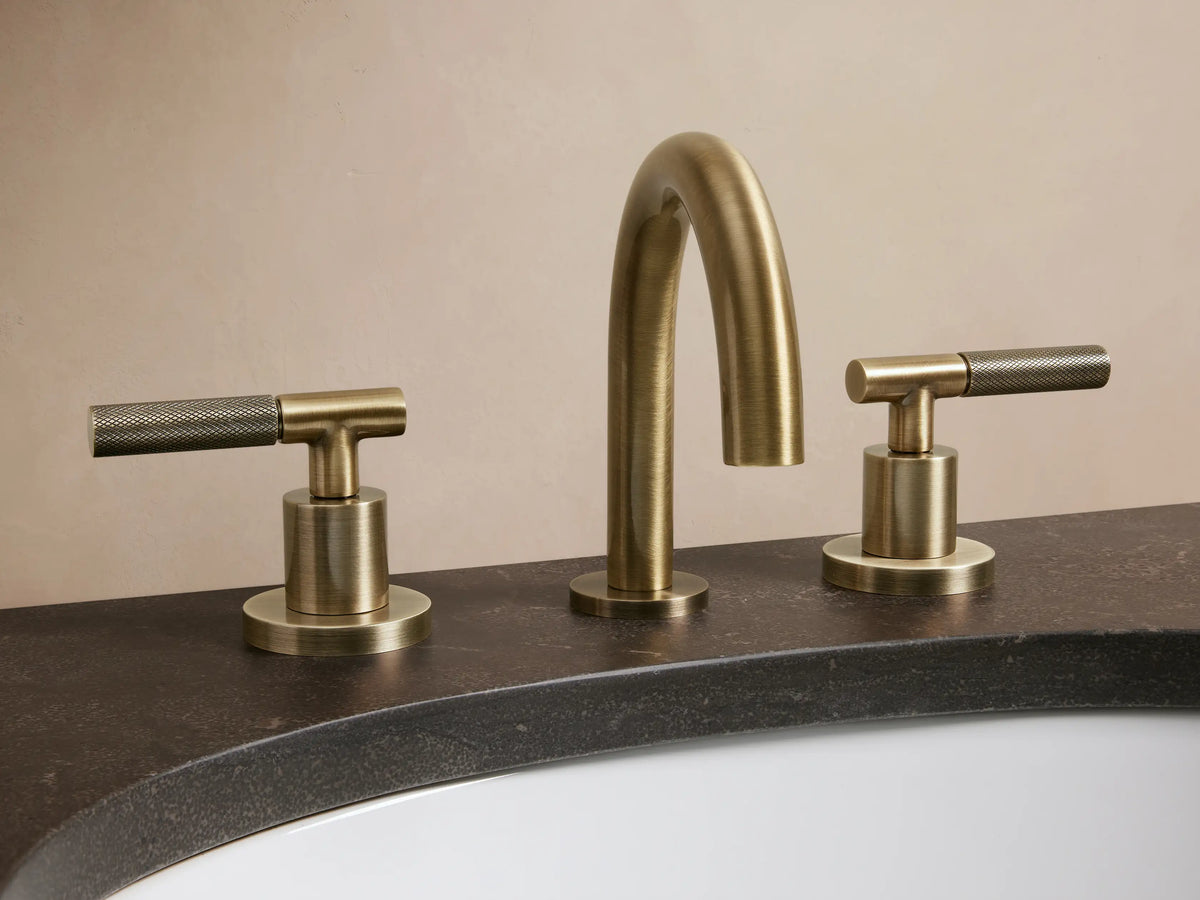 Crewe Knurled Faucet in antique brass finish with two handles, mounted on a white marble countertop beside a folded towel.