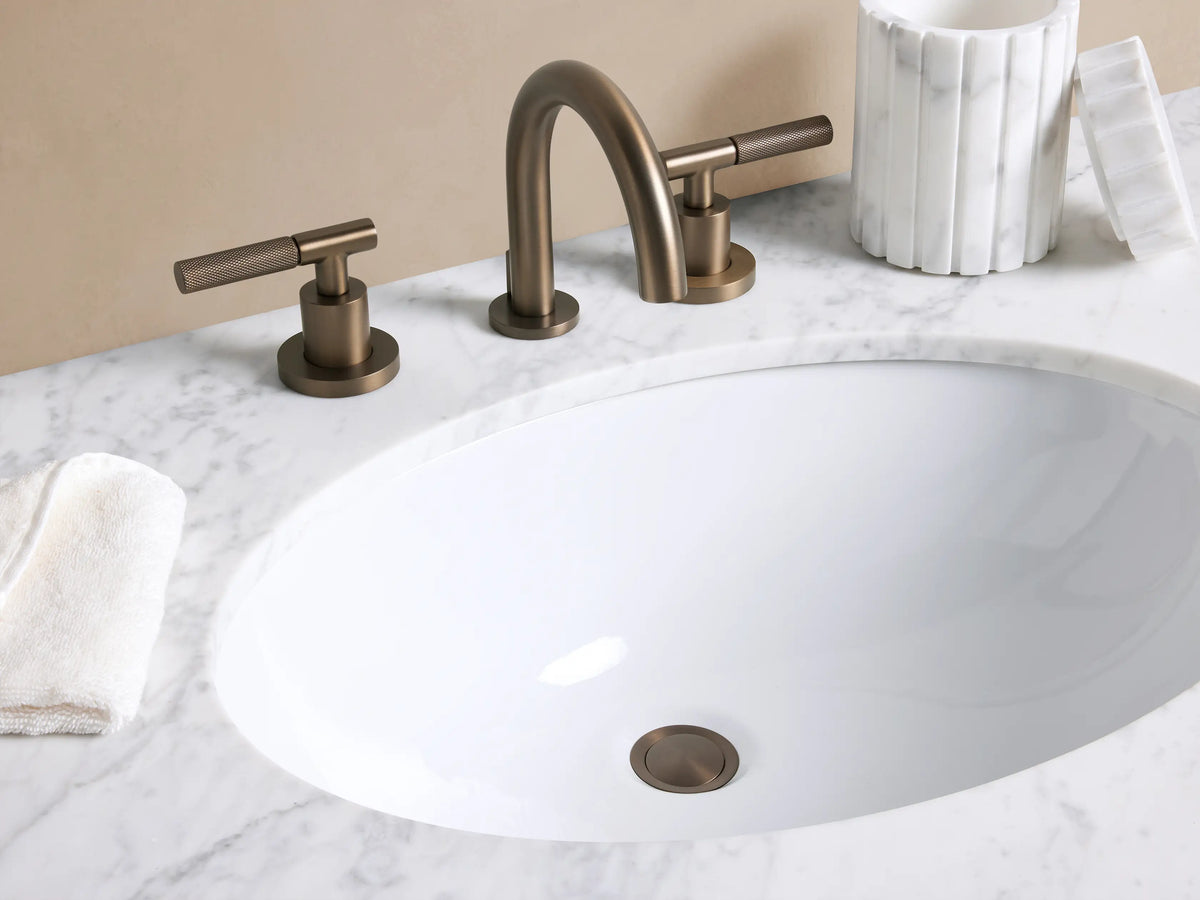 Crewe Knurled Faucet in Bronze: Three-piece widespread bronze faucet with a gooseneck spout & knurled T-handles on white marble.