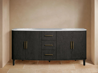 Danny Double Vanity: dark black wood with white Carrara marble top, two sinks, brass faucets & hardware. One door slightly ajar, towels inside.