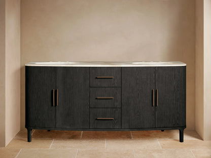 Danny Double Vanity, dark oak with curved ends & light marble top. Two sinks, bronze faucets, left door ajar with towels.