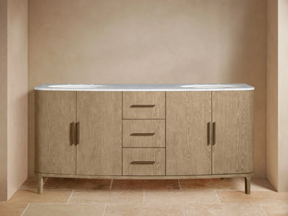 Danny Double Vanity: light oak wood, white marble top, dual sinks, bronze hardware, curved base. Left cabinet open with towels.