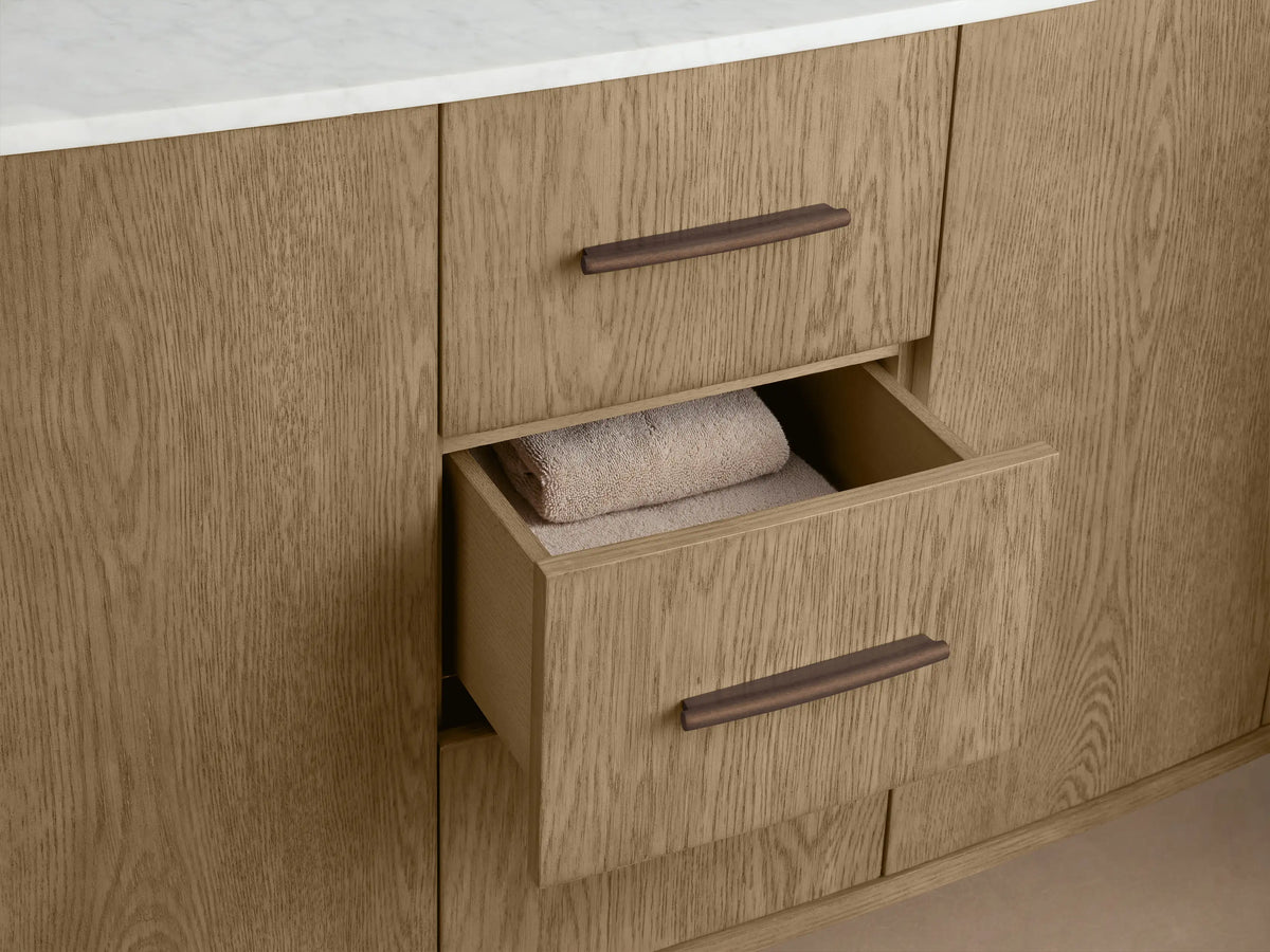 Danny Double Vanity close-up: light oak cabinet door ajar, showing rounded edges, a dark handle, shelves with folded beige towels & a small box.