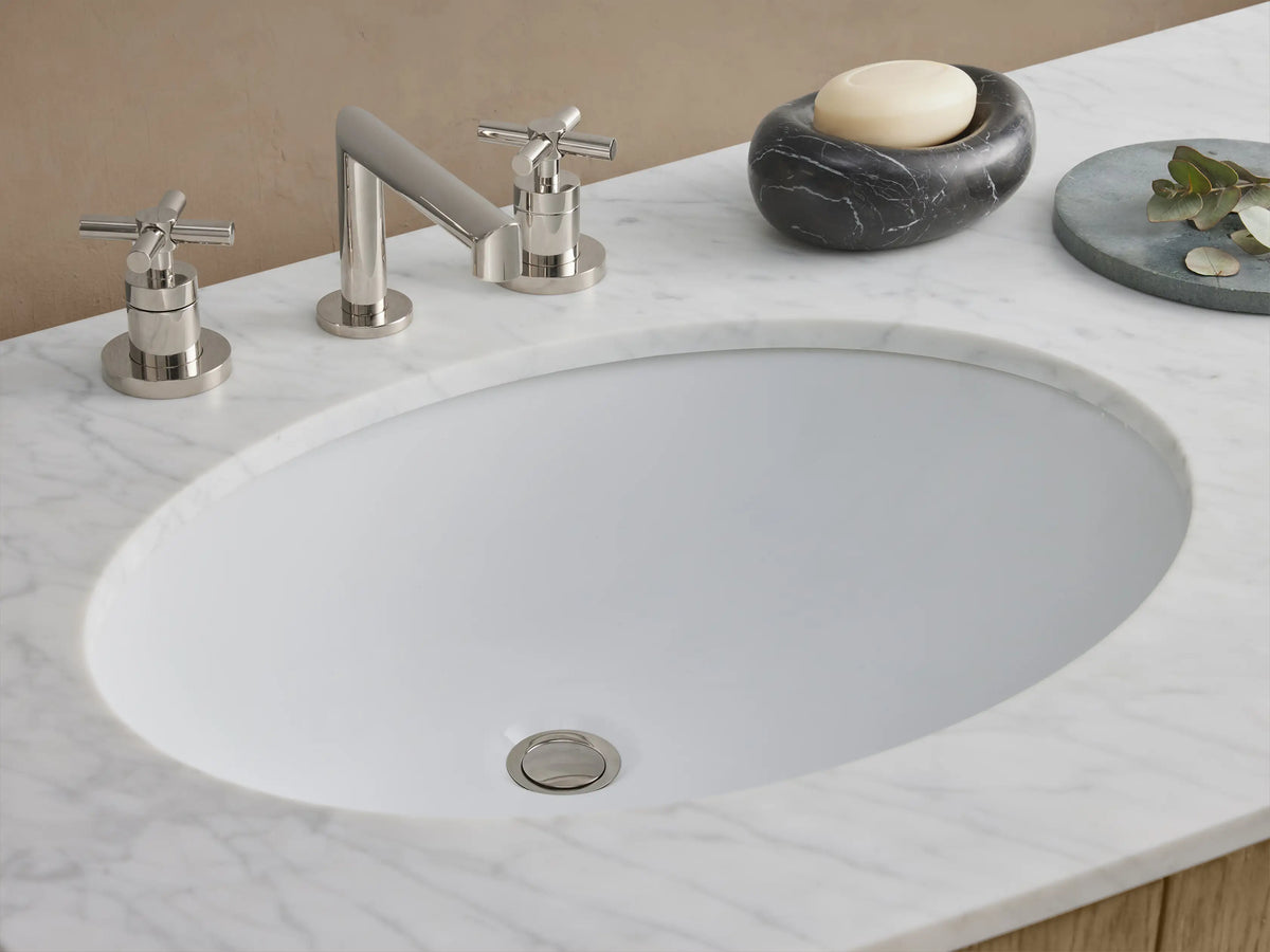 Danny Double Vanity made of oak with a marble top. Features oval sinks, central drawers, and doors with brass handles.