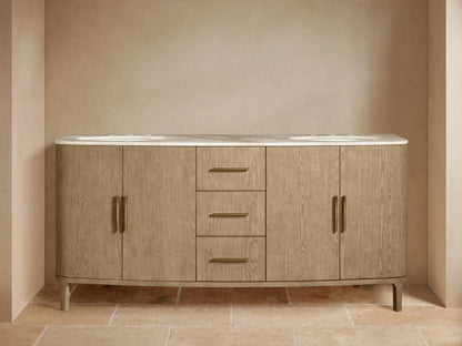 Danny Double Vanity in light oak with two oval ceramic sinks and brass hardware. Features open shelves, drawers, and cabinets.