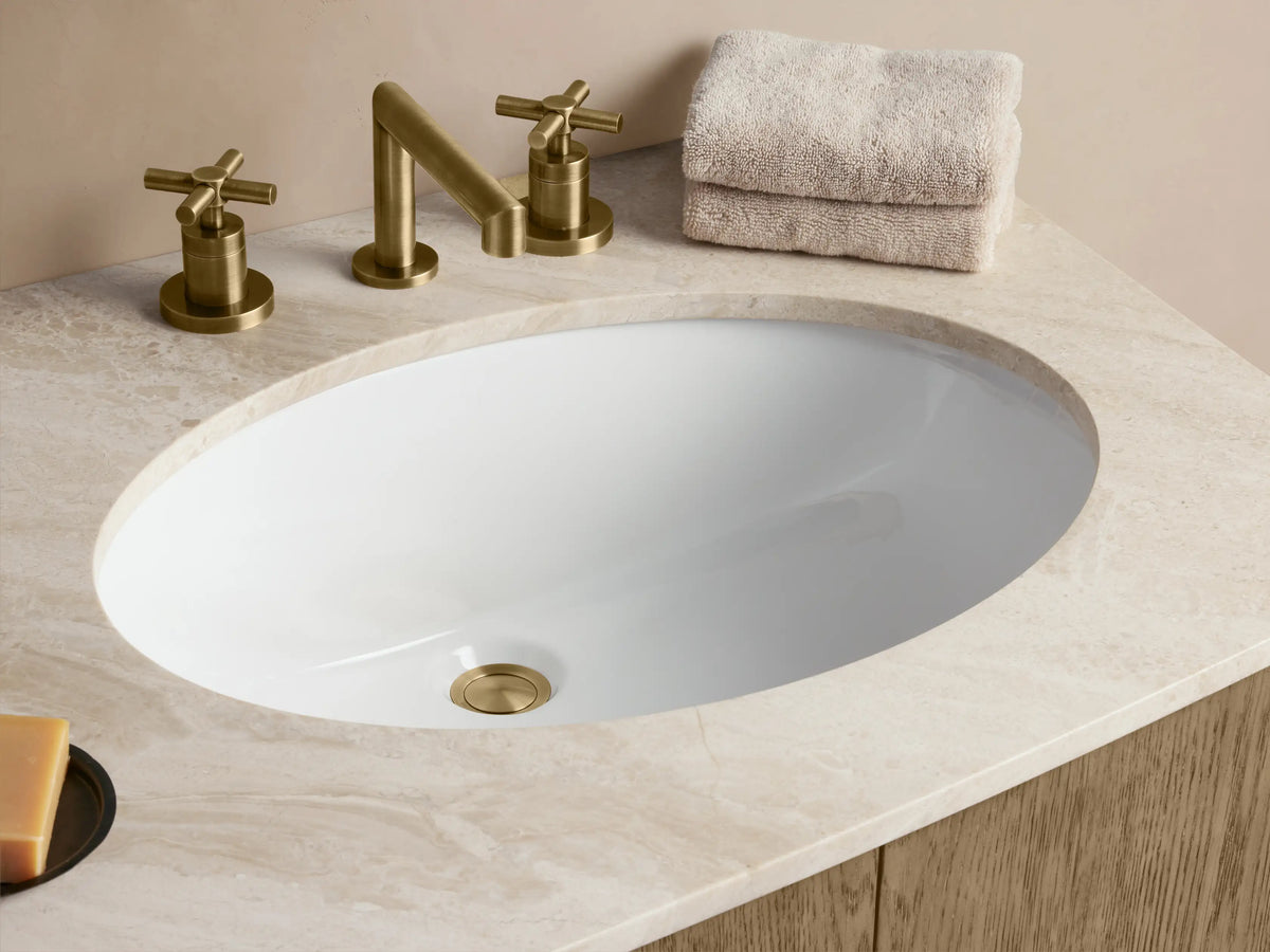 Danny Double Vanity made of oak wood, featuring a stone top with two ceramic sinks. Three center drawers and two side doors have brass handles.