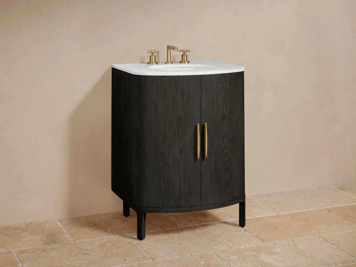 Danny Powder Vanity: dark oak, curved cabinet, white marble top, oval sink, brass faucet, two vertical brass door handles.