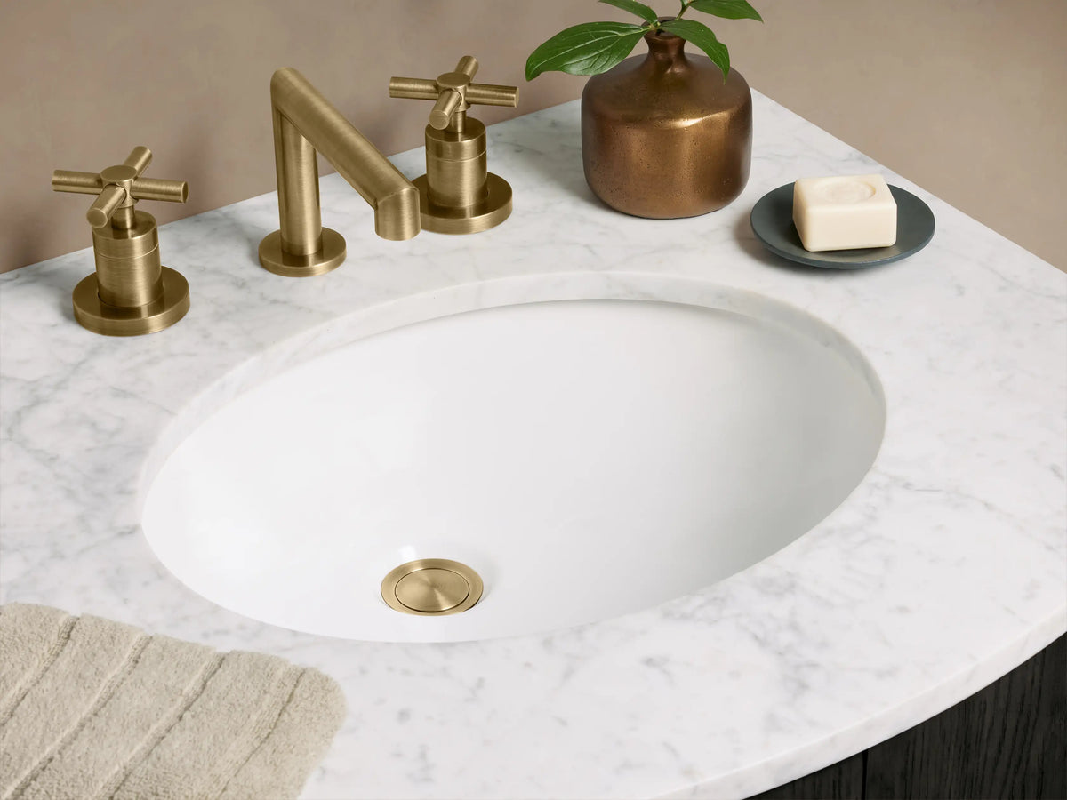A dark-stained oak wood Danny Powder Vanity with a white Carrara marble top, brass faucet, and two brass door handles.