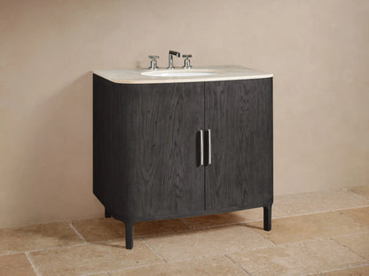 Open Danny Single Vanity cabinet in dark oak showing two shelves. Towels and a marble box on top shelf, dark container on bottom shelf. Chrome handle on left door.