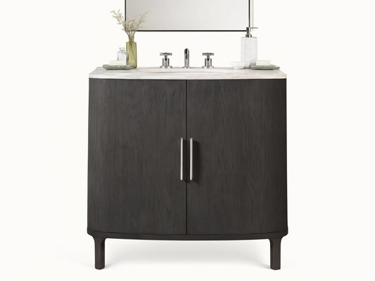 Danny Single Vanity in dark oak with rounded edges, a white stone top, two metallic handles, and a ceramic sink, set against a beige tile wall.