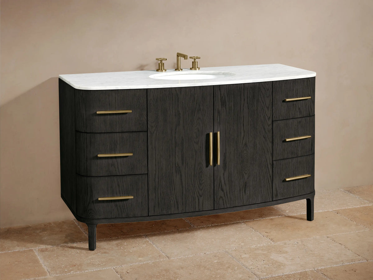 Close-up of Danny Wide Single Vanity. Dark oak door ajar showing shelves with towels & bottles. Brass bar pulls on doors & drawers.