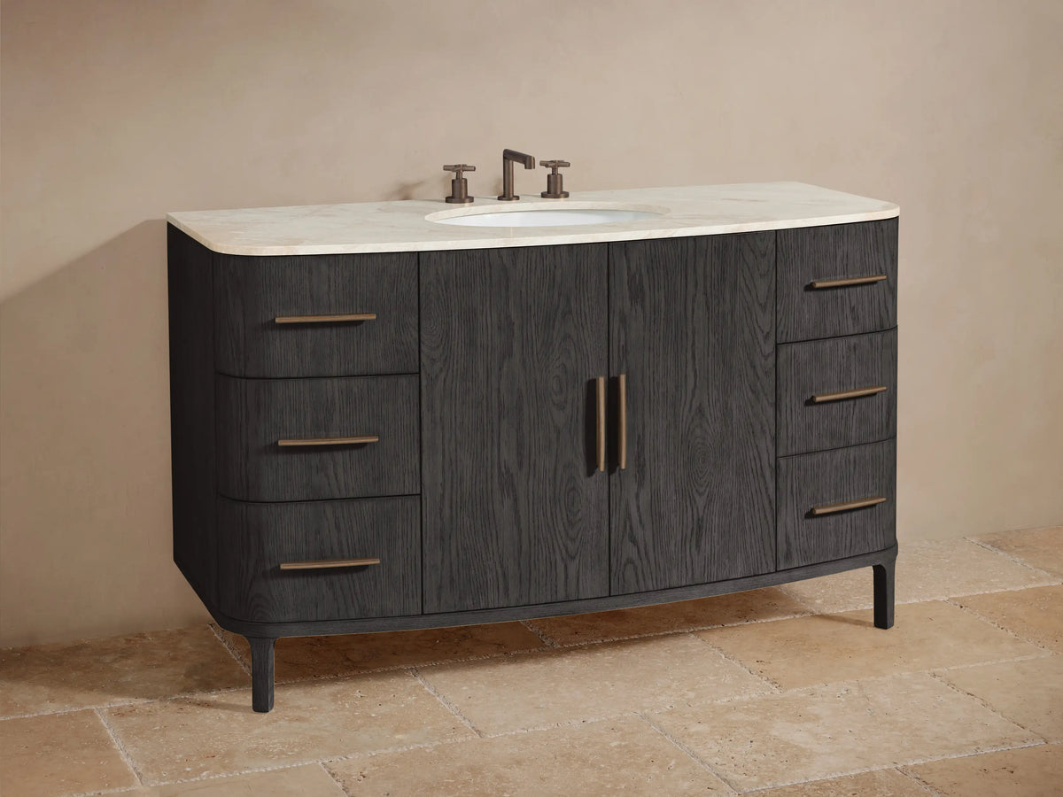 Partial view of Danny Wide Single Vanity in dark gray oak. Open cabinet reveals shelf with jars and towels; drawers with bronze bar pulls.