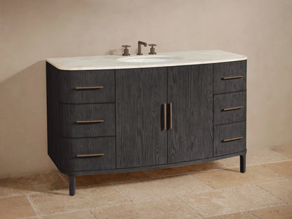 Partial view of Danny Wide Single Vanity in dark gray oak. Open cabinet reveals shelf with jars and towels; drawers with bronze bar pulls.