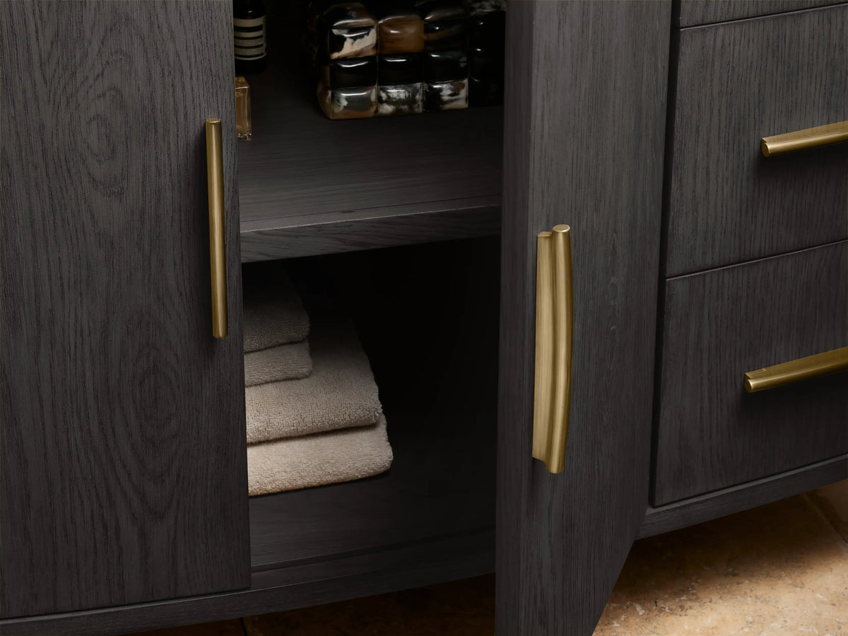 Danny Single Wide Vanity with dark oak wood finish, open drawer, towel inside, and gold-colored handles; beige stone top visible.