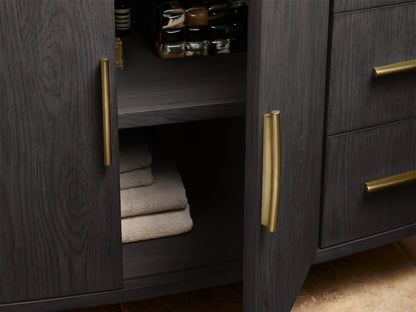 Danny Single Wide Vanity with dark oak wood finish, open drawer, towel inside, and gold-colored handles; beige stone top visible.