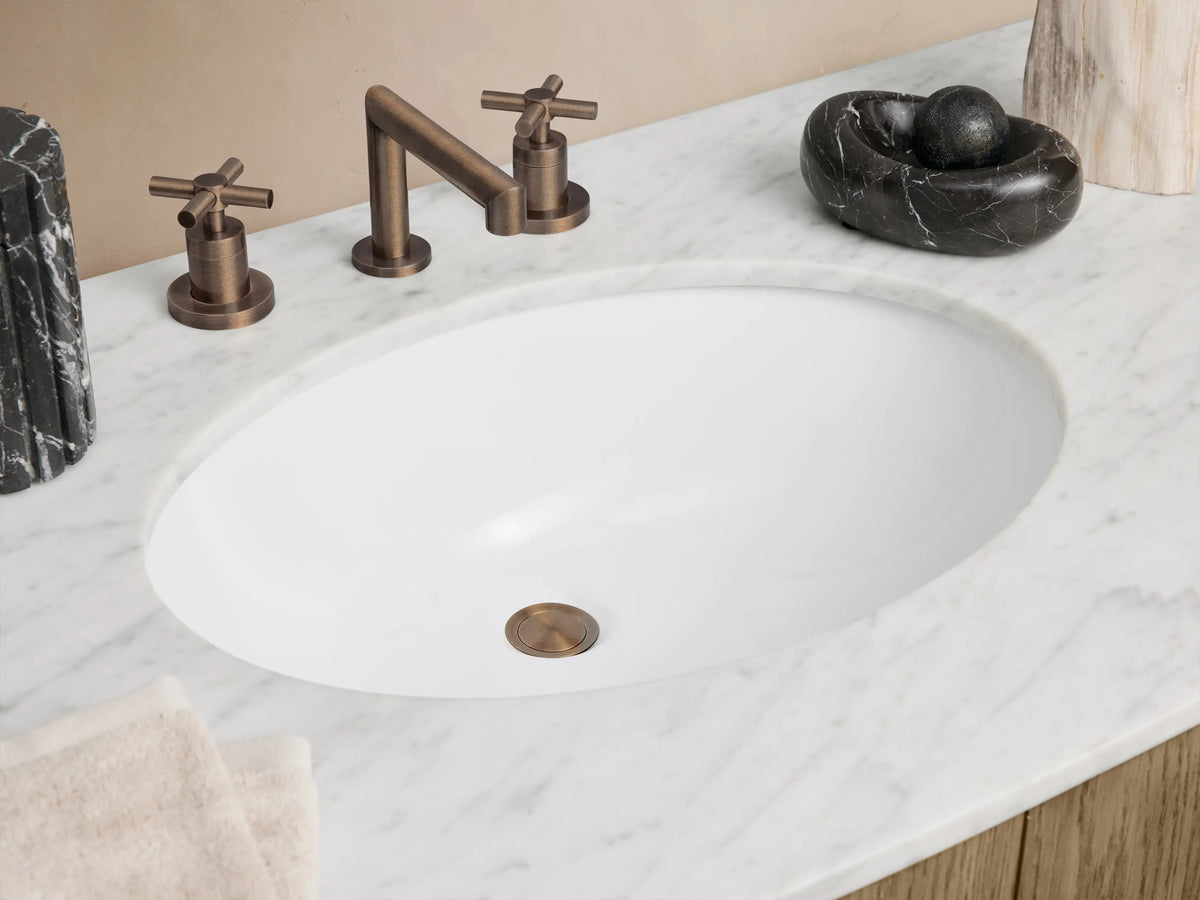 Light brown wood Danny Wide Single Vanity with white oval sink, white top, 2 doors, 6 drawers with bronze handles, curved front.