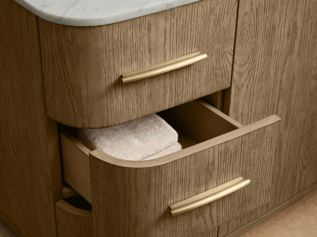 Oval undermount ceramic sink set in a Carrara marble countertop with antique brass fixtures, showing elegant design details.