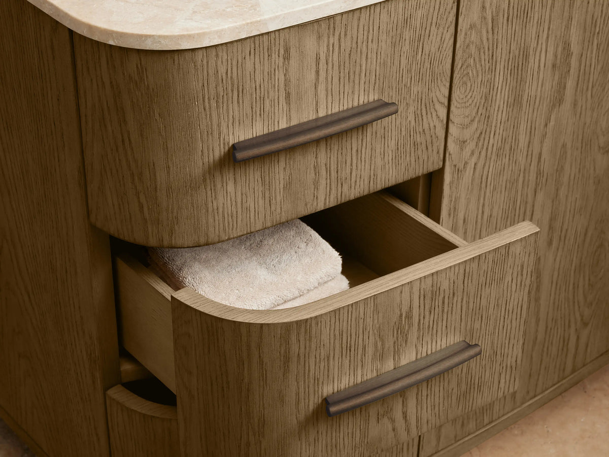 Close-up of Danny Wide Single Vanity in light oak, showing two open cabinet doors with bronze pulls, revealing towels & bottles.