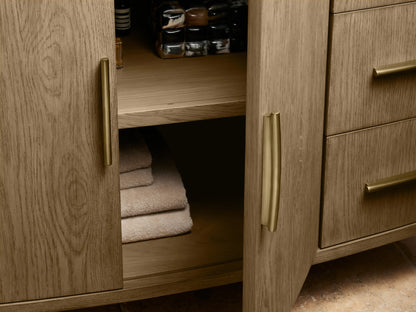 Danny Single Wide Vanity with curved oak wood finish, open drawer revealing a towel, and brass hardware on soft-close glides.