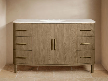 Oval ceramic undermount sink in honed stone top with antique brass faucet; beige towel and decorative soap.