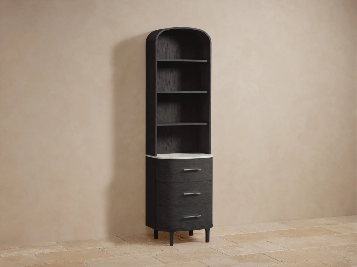 Angled view of black oak Danny Bath Cabinet with two shelves. White towels on top. Plant & candle on white marble surface below.
