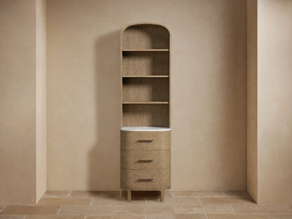 Danny Bath Cabinet: Tall, light oak, arched top, 3 open shelves, 3 drawers, white marble top, bronze hardware on beige wall.
