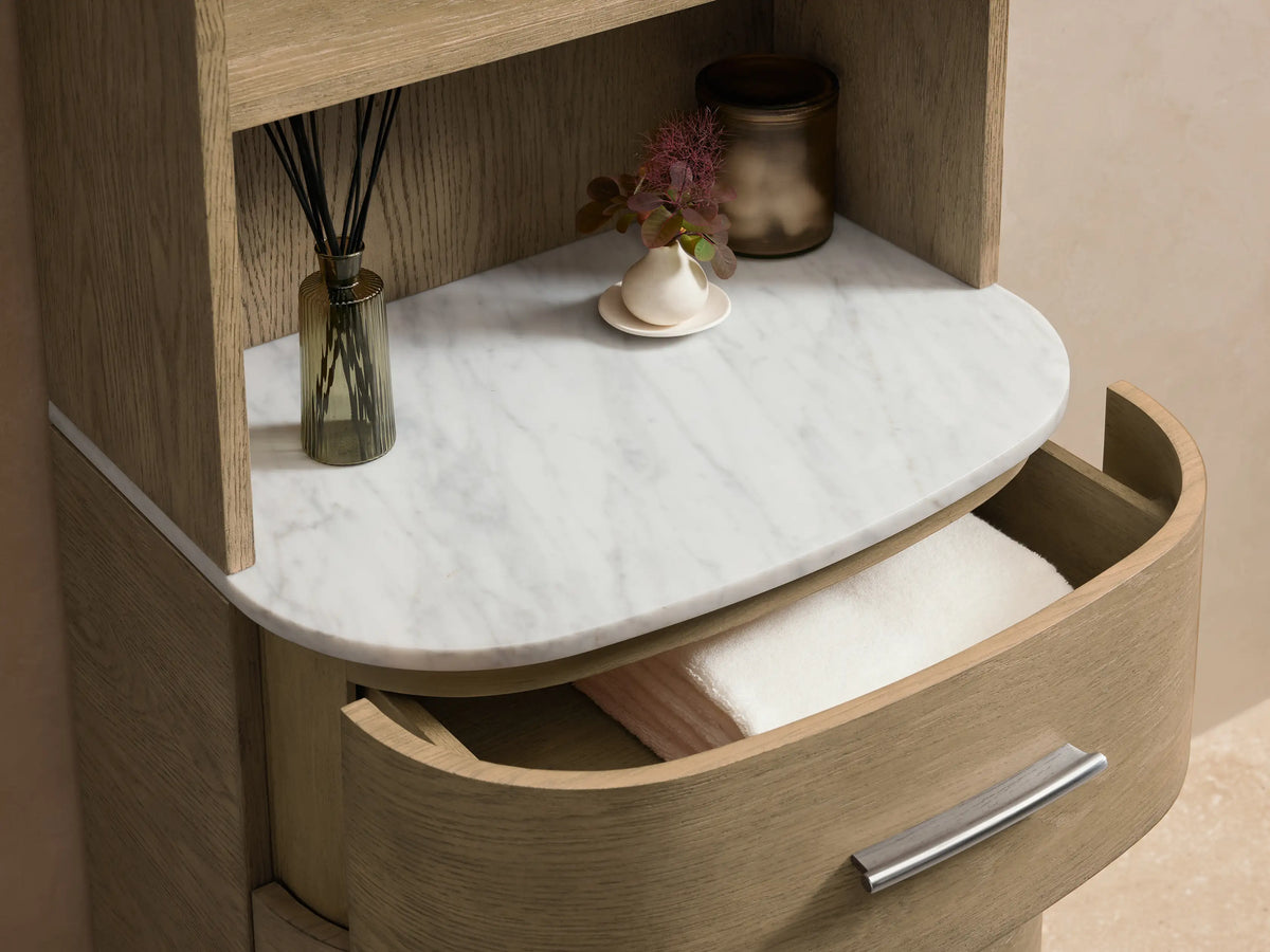Danny Etagere in light oak with three open shelves, Carrara marble top, and three drawers with brass hardware on light brown flooring.