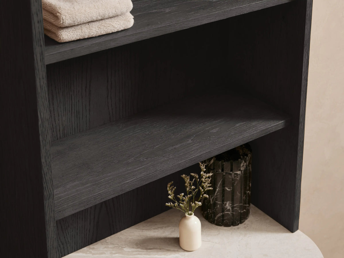 Dark oak Danny Bath Cabinet, curved light stone top, open drawer with towels, bronze handle, vase, black soap dispenser.
