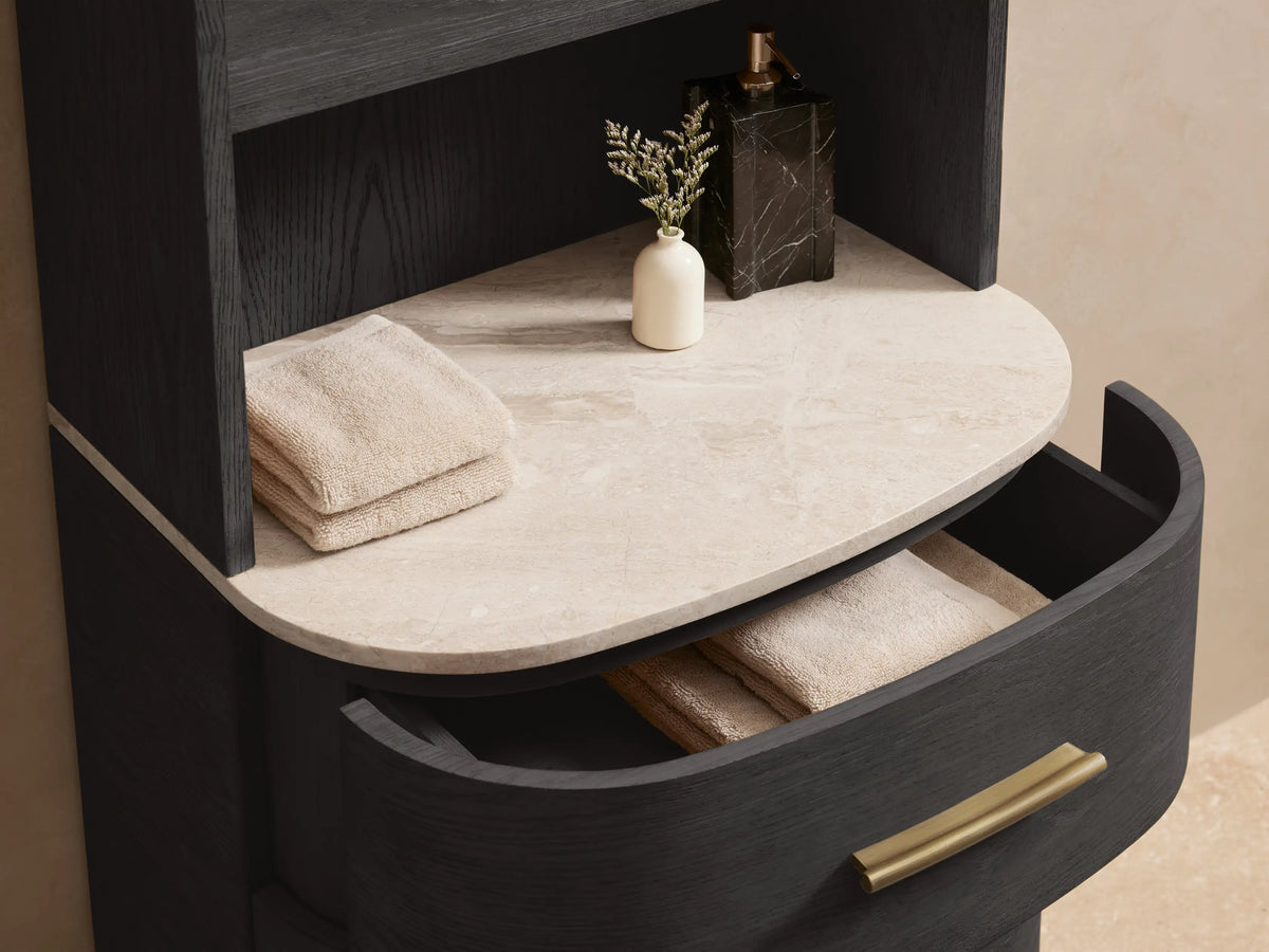 Danny Etagere made of dark oak wood with a curved top, three drawers with brass handles, and stone surface, set against a beige wall.