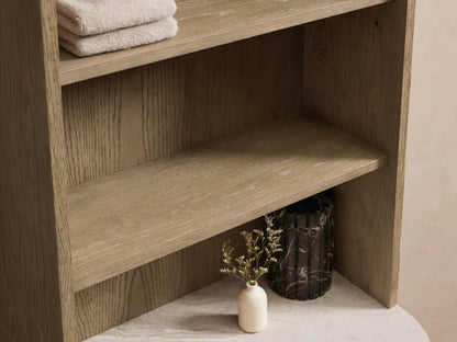 Danny Bath Cabinet, light oak with curved marble top, open drawer with towels, vase, and black soap dispenser.