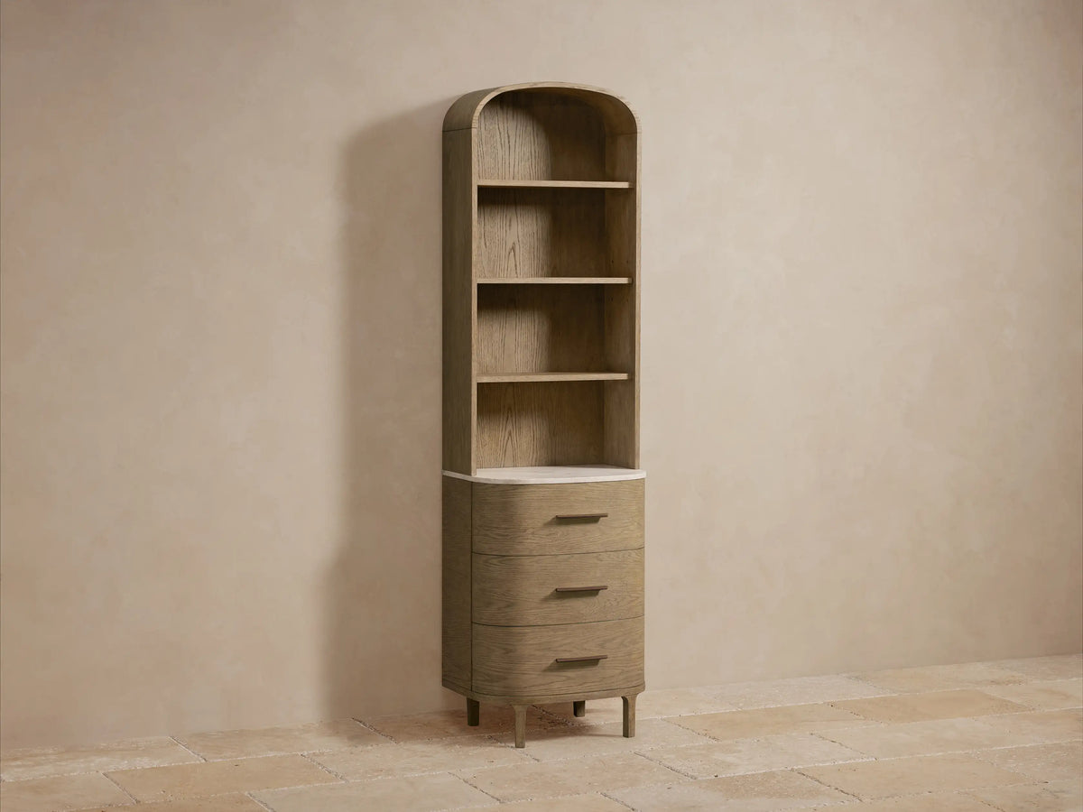Close-up of light oak Danny Bath Cabinet shelves. Top shelf has beige towels; bottom shelf has a white vase, dried flowers, and a black marble container.