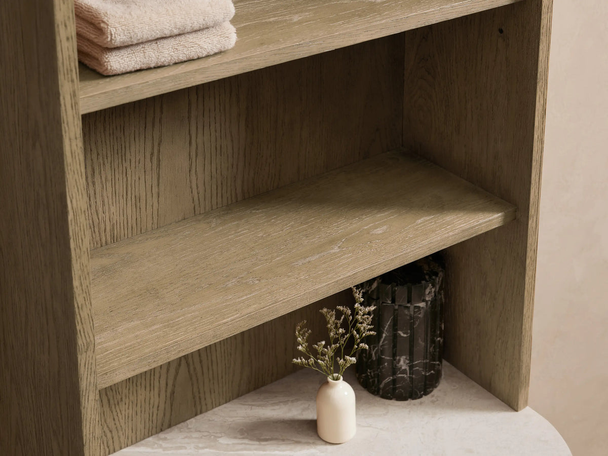 Danny Etagere with open drawer, stone top holding folded towels, vase with plant, and soap pump; oak wood finish.