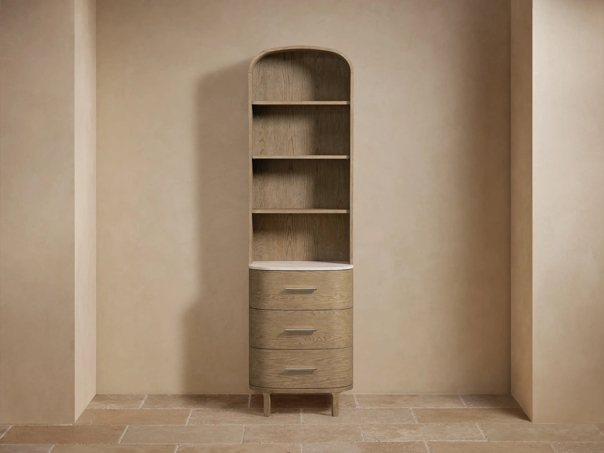 Danny Etagere made of oak wood with two shelves; top shelf holds folded towels, bottom shelf holds vase with flowers on stone top.