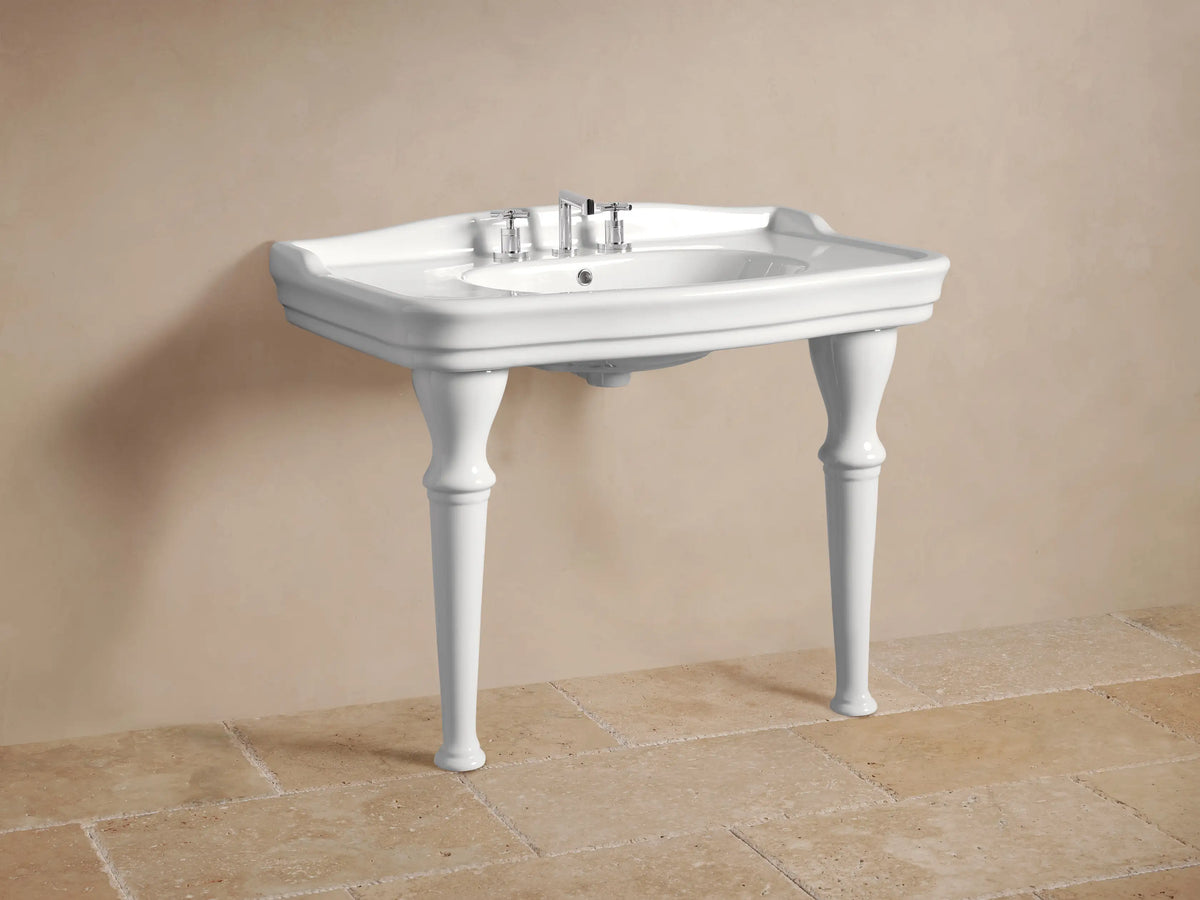 Close-up of a glossy white ceramic Eloise Single Washstand with an integrated sink and wide deck, against a light brown wall.
