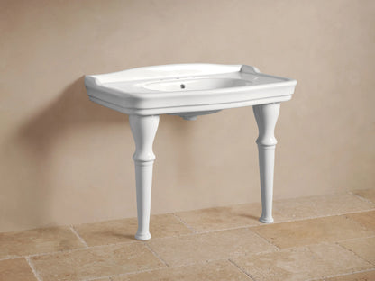 White Eloise Single Washstand with integrated sink, four elegant turned legs, and chrome faucets, against a light wall & tiled floor.