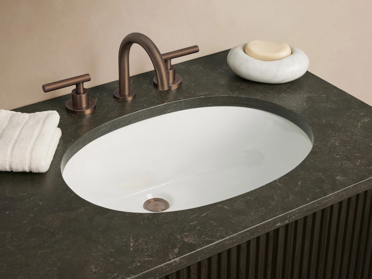 Finnley Double Vanity: Dark brown fluted wood double vanity with a dark gray stone top, two white oval sinks, and bronze handles.