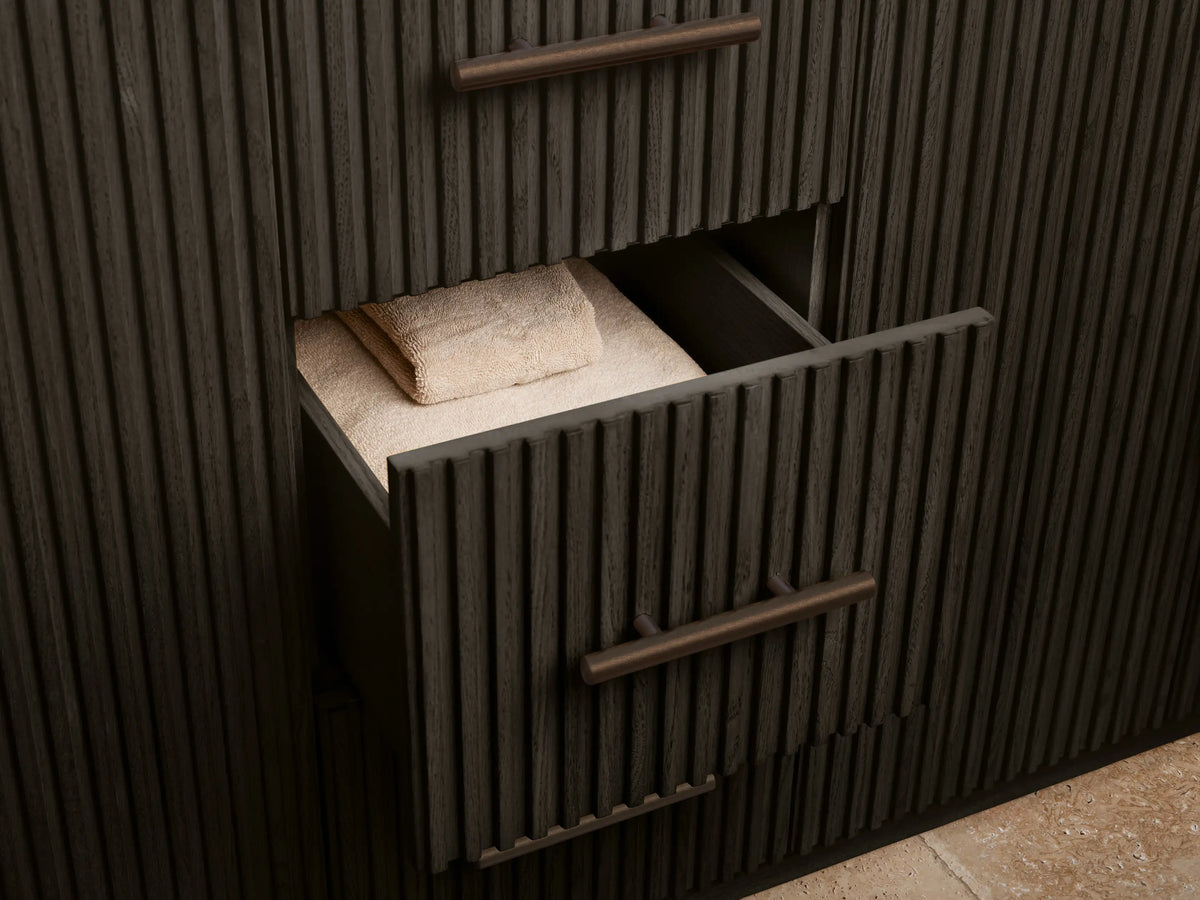 Finnley Double Vanity: Dark fluted cabinet door with antique bronze pull, partially open. Inside, a shelf with a sponge in a bowl & white towels.