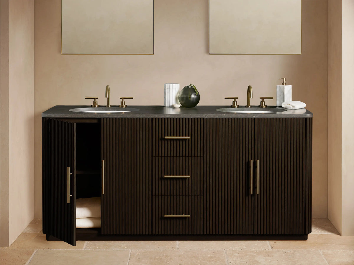 Finnley Double Vanity, dark brown fluted wood, gray stone top with two white sinks, gold faucets, & antique brass hardware.