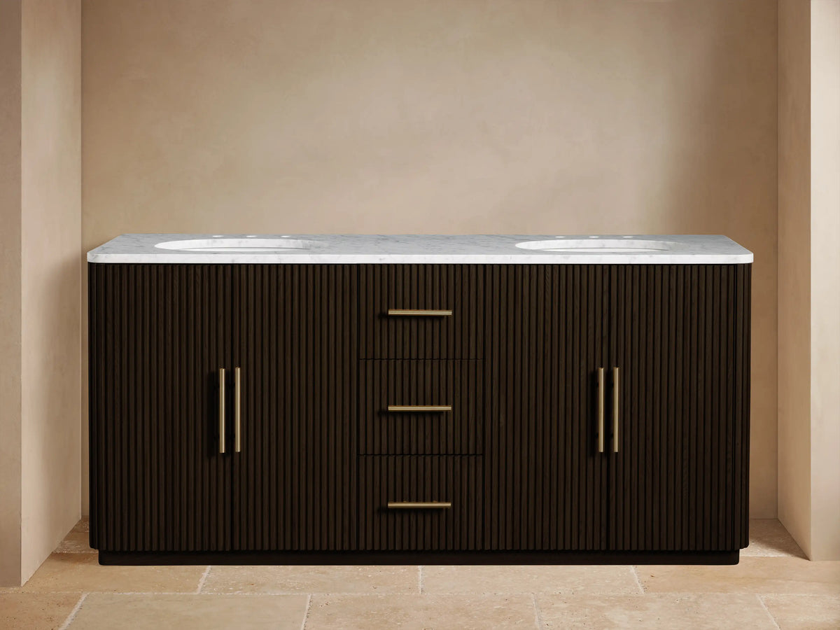 Finnley Double Vanity: dark fluted wood, white marble top, 2 sinks, brass faucets & handles. Left cabinet open showing towels.
