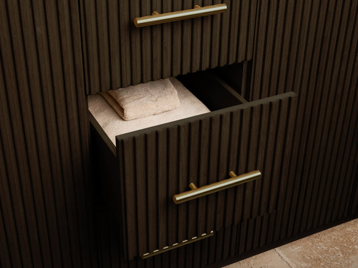 Close-up of Finnley Vanity's dark ribbed wood cabinet door open, showing golden handle, natural sponge in bowl, and white towels inside.