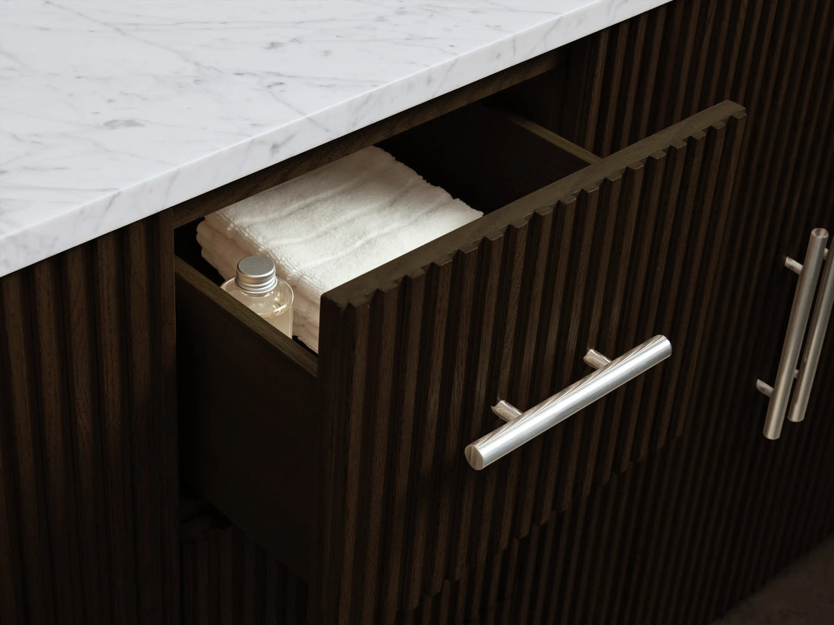 Finnley vanity cabinet: open dark brown fluted door with brass handle. Inside, a shelf holds a natural sponge; white folded towels below.