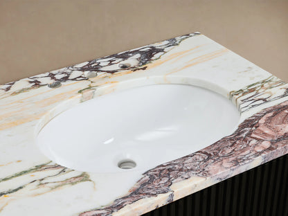 Close-up Finnley Vanity sink: white oval basin, antique brass faucet on multi-color veined marble countertop, with soap dispenser & towel.