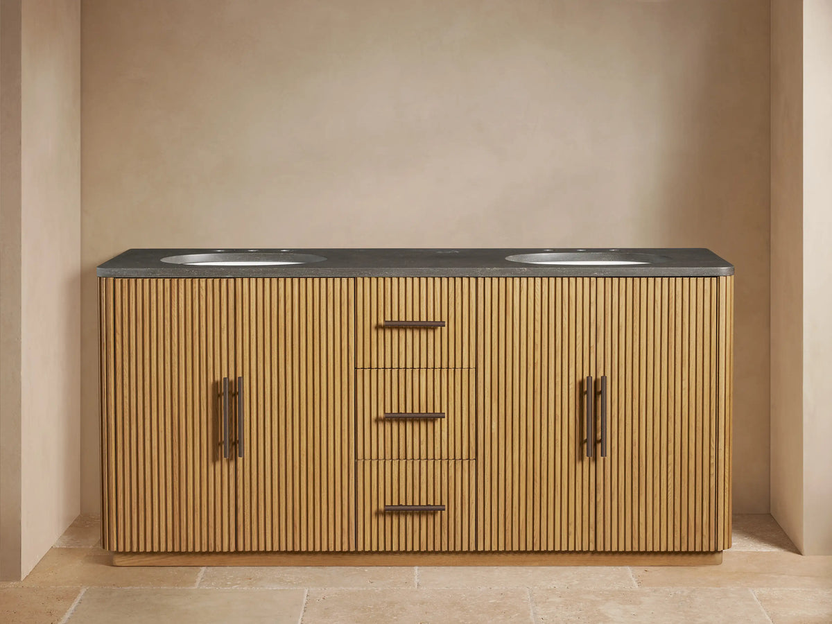 Finnley Double Vanity: Light oak wood with fluted doors/drawers, dark bluestone top, two white sinks, dark bronze faucets. Left door open with towels.