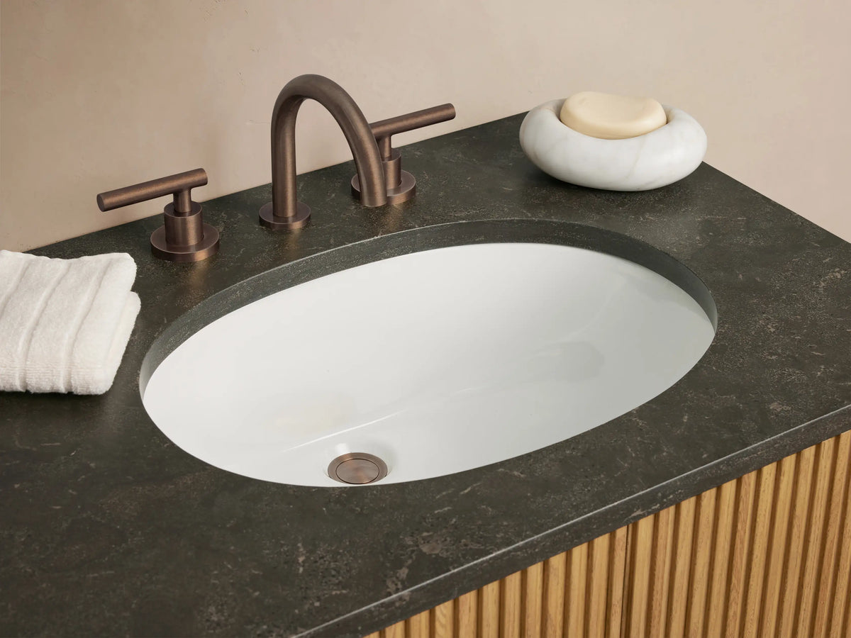 Finnley Double Vanity: light oak slatted cabinet, dark bluestone countertop with two oval white sinks, and dark bronze hardware.