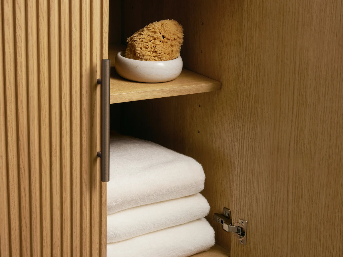 Close-up of Finnley Double Vanity, light oak with fluted texture. A drawer is open, revealing light towels, with dark bar pulls.