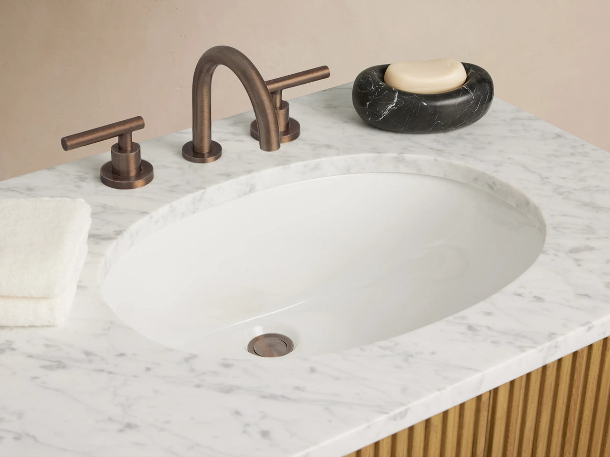 Finnley Double Vanity: light oak wood with reeded texture, white marble top, two oval sinks, 4 doors, 3 drawers, bronze handles.