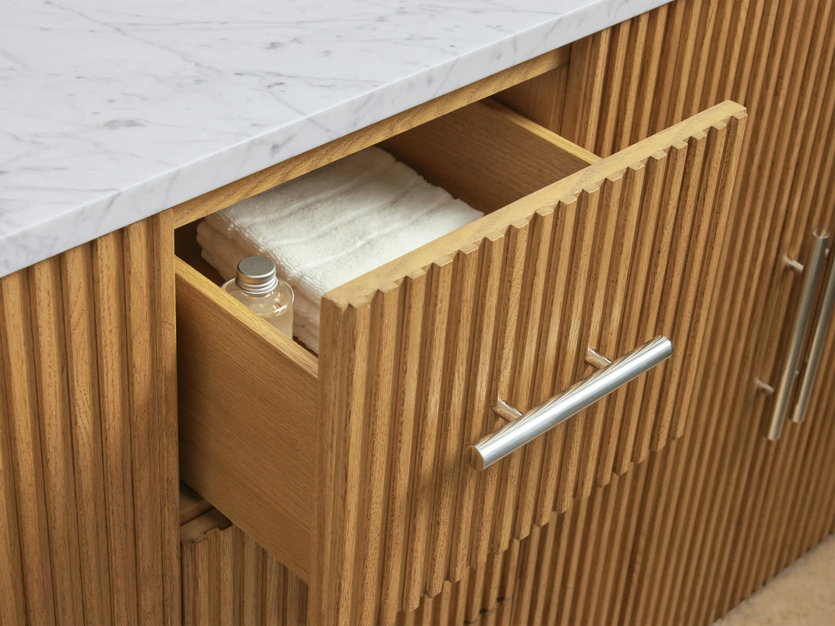 Open cabinet showing oak wood grain door with silver handle, shelves holding folded towels and toiletry items on a circular tray.