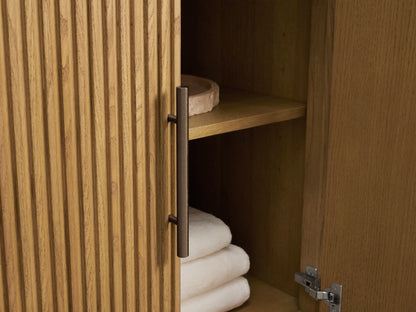 Close-up of Finnley Double Vanity: light oak wood with reeded texture, reddish-white veined marble top. One drawer open with towels & bottles.